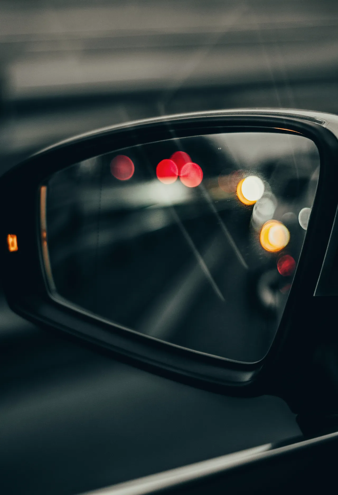 Retrovisor exterior de un coche gris oscuro de noche, con las luces de la calle desenfocadas en el espejo