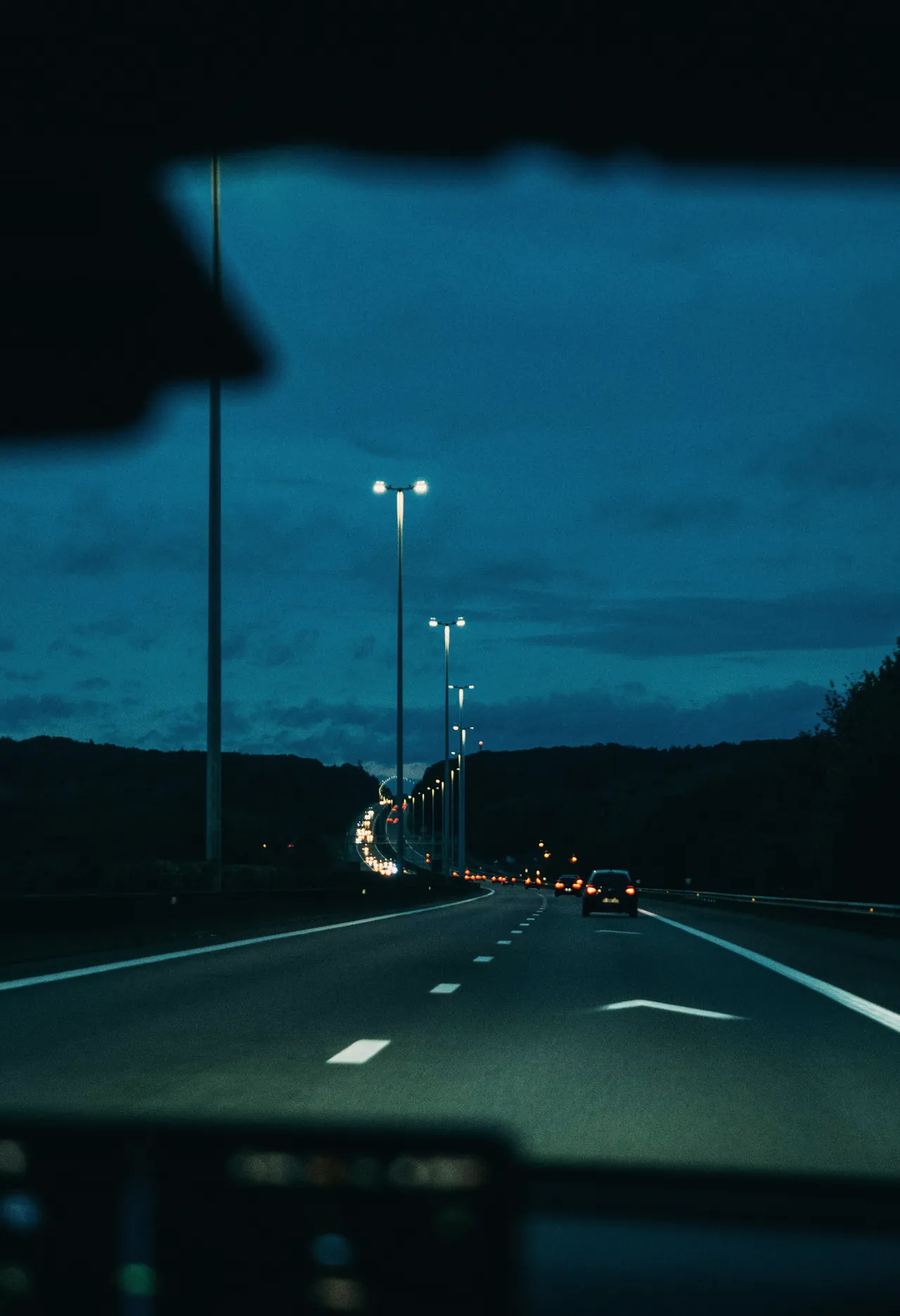 Autovía a la hora azul vista desde el asiento del conductor, con las farolas encendidas y los pilotos rojos de los coches de delante