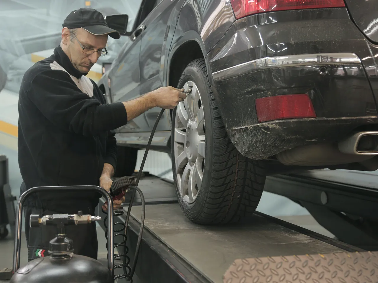 Técnico con gorra comprobando la presión de la rueda trasera de un SUV gris oscuro en un taller luminoso