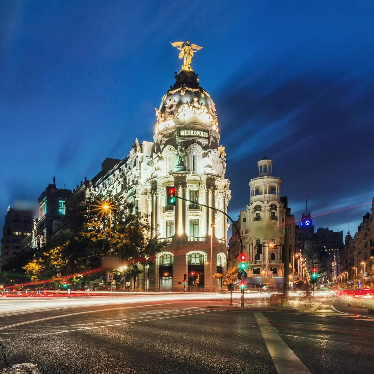 El edificio Metrópolis iluminado a la hora azul, con estelas rojas y blancas del tráfico en el cruce de Alcalá con la Gran Vía